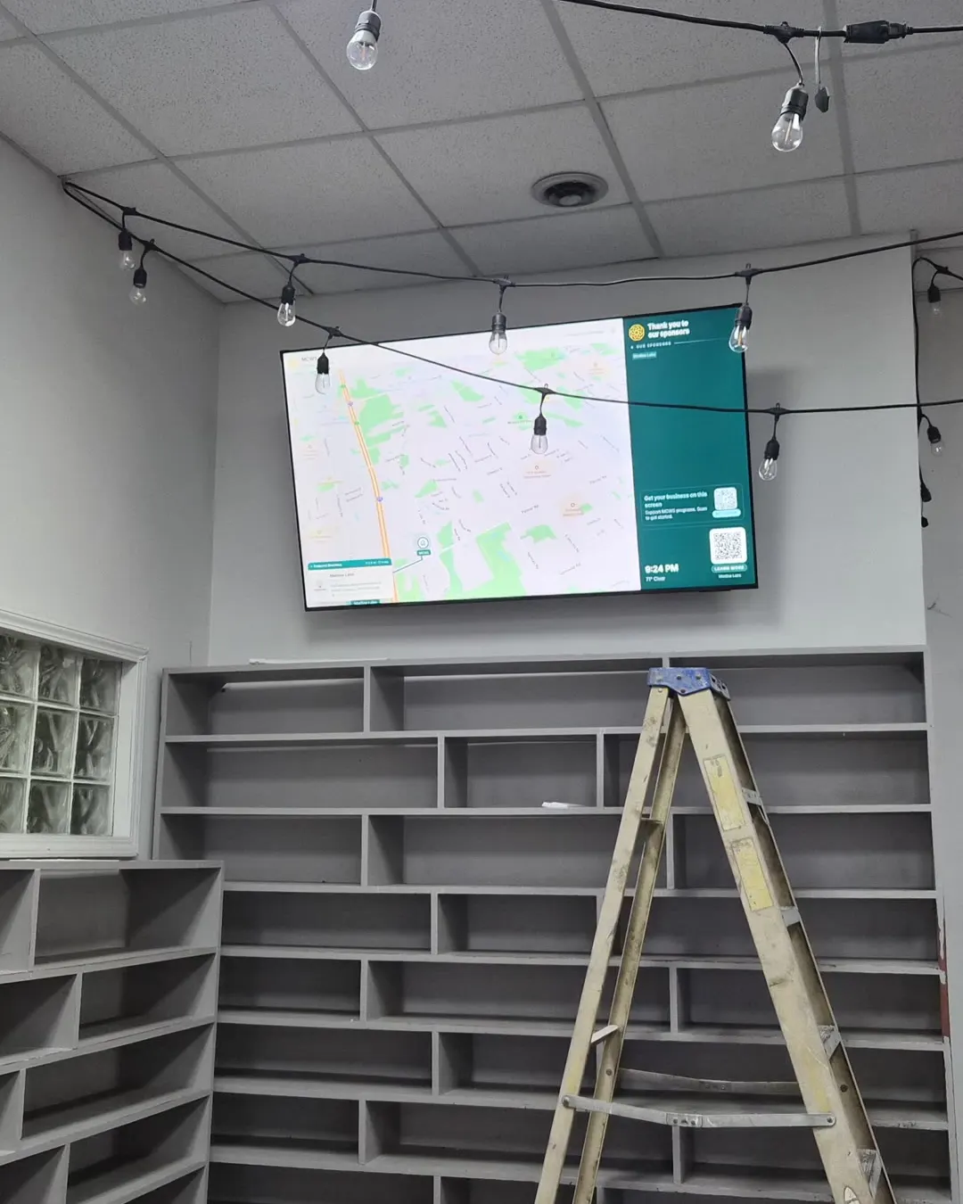 The UnityMap display mounted high on the wall at MCWS, above rows of empty shoe racks, with string lights across the ceiling